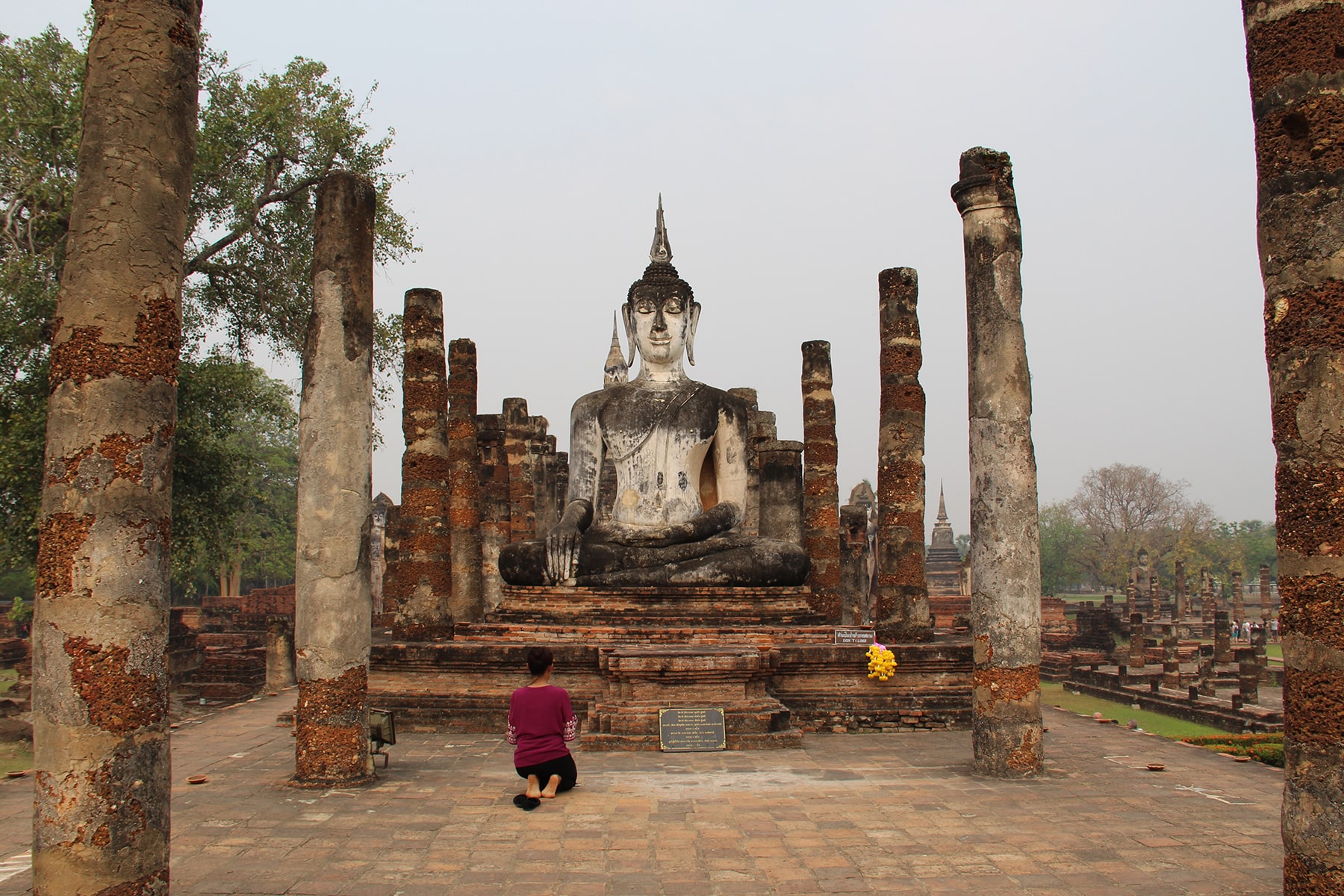 Femme priant devant la statue blanche de Bouddha entre ruines de colonnes dans le hall d'ordination au Wat Mahathat - Parc historique de Sukhothaï