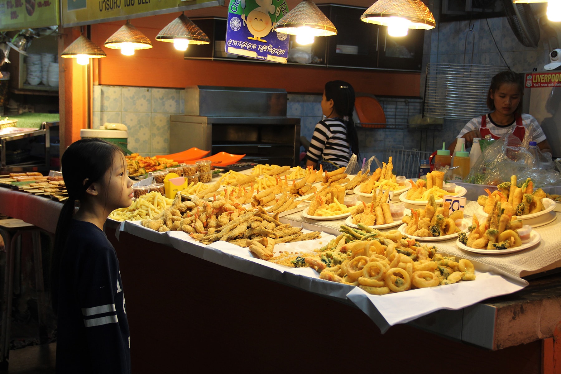 A girl standing in front of a fried food stand in the night market of Chiang Rai